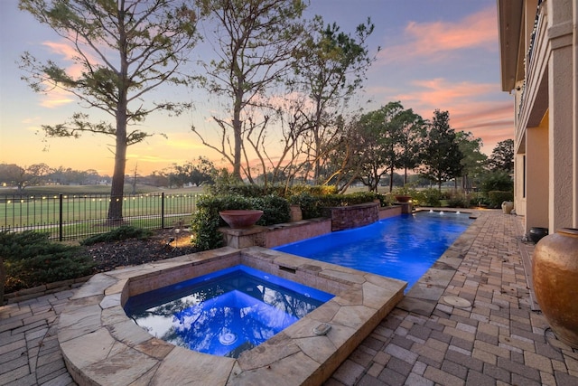 pool at dusk with an in ground hot tub and a patio