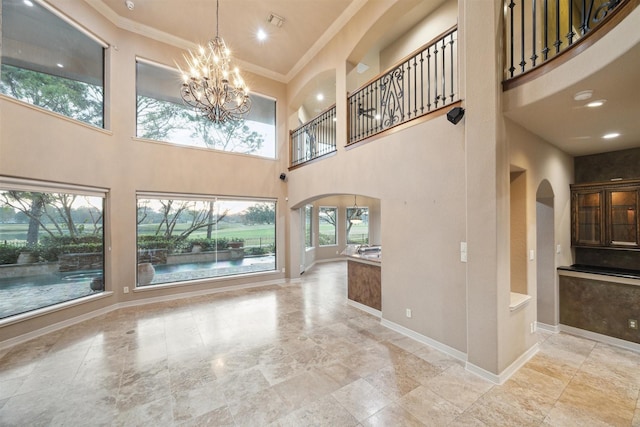 unfurnished living room featuring a chandelier, a towering ceiling, and ornamental molding