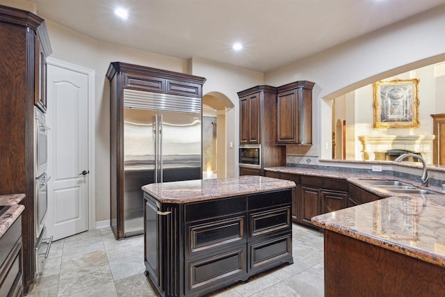 kitchen with built in appliances, a center island, dark brown cabinetry, and sink