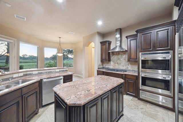 kitchen featuring appliances with stainless steel finishes, sink, wall chimney range hood, a center island, and hanging light fixtures