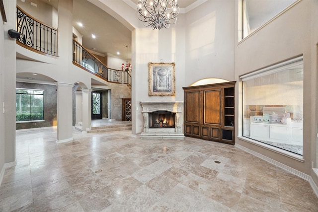 unfurnished living room featuring a towering ceiling, ornamental molding, and decorative columns