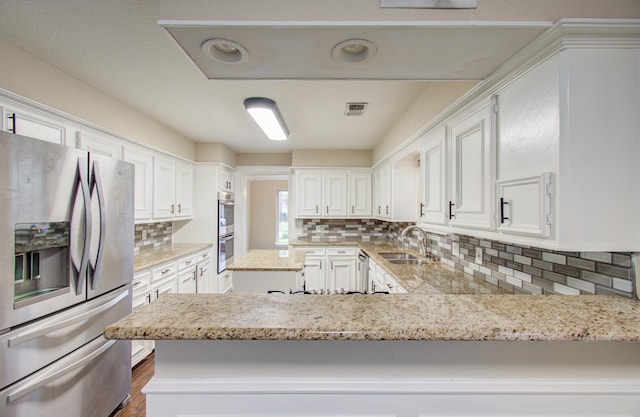 kitchen with white cabinets, sink, appliances with stainless steel finishes, tasteful backsplash, and kitchen peninsula