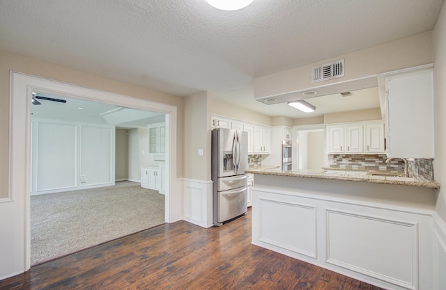 kitchen with tasteful backsplash, a textured ceiling, stainless steel appliances, white cabinets, and dark hardwood / wood-style floors