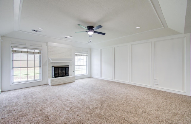 unfurnished living room with ceiling fan, plenty of natural light, light colored carpet, and a brick fireplace