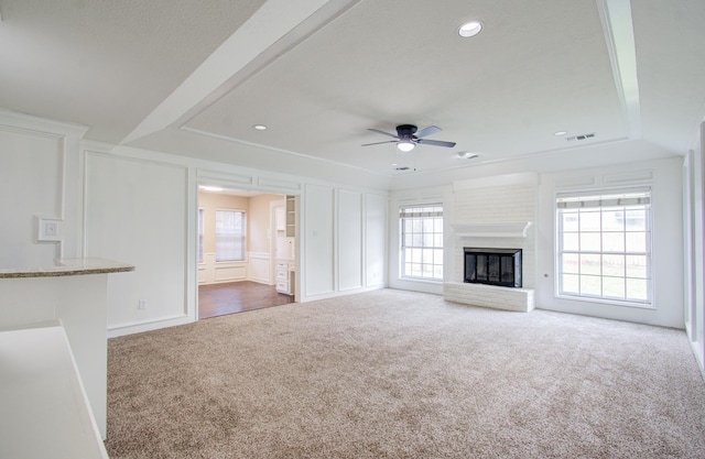 unfurnished living room with dark colored carpet, ceiling fan, a healthy amount of sunlight, and a brick fireplace