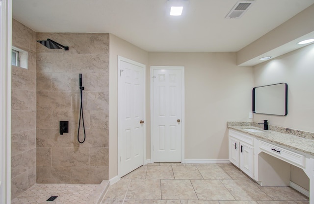 bathroom with tile patterned flooring, vanity, and a tile shower