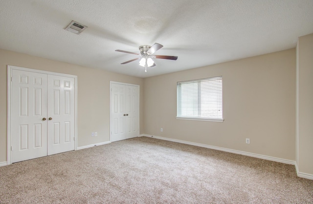 unfurnished bedroom with carpet, ceiling fan, a textured ceiling, and multiple closets