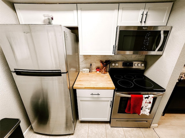 kitchen with white cabinets, tasteful backsplash, butcher block countertops, light tile patterned flooring, and stainless steel appliances