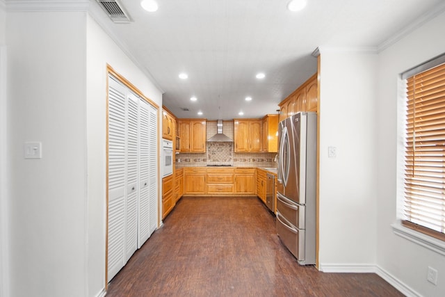 kitchen with white oven, tasteful backsplash, wall chimney range hood, ornamental molding, and stainless steel refrigerator