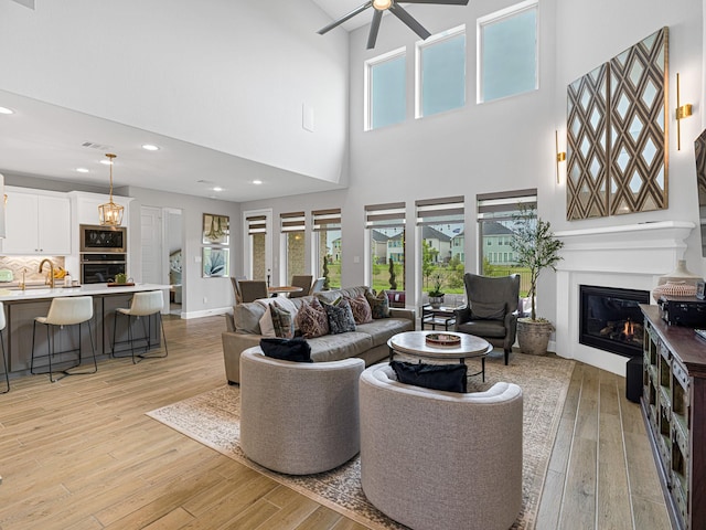 living room featuring ceiling fan, a towering ceiling, sink, and light hardwood / wood-style flooring