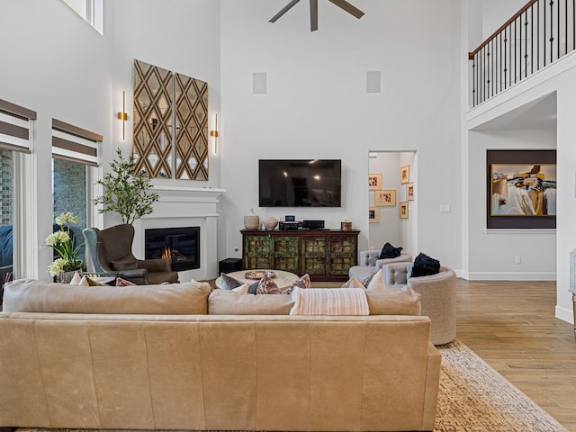 living room with ceiling fan, a towering ceiling, and light hardwood / wood-style floors