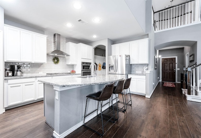 kitchen with wall chimney exhaust hood, dark hardwood / wood-style floors, white cabinetry, and an island with sink