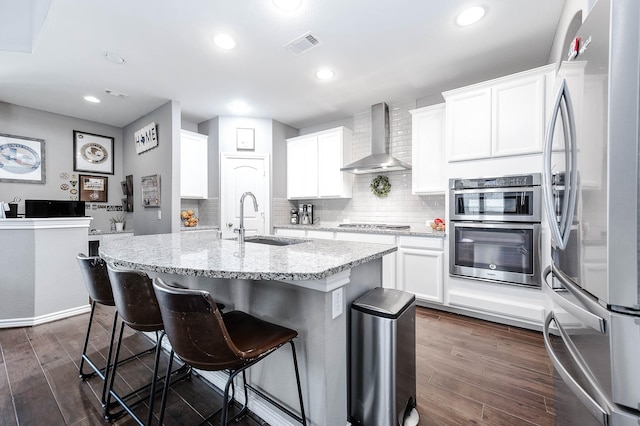 kitchen with white cabinets, wall chimney range hood, sink, dark hardwood / wood-style flooring, and stainless steel appliances