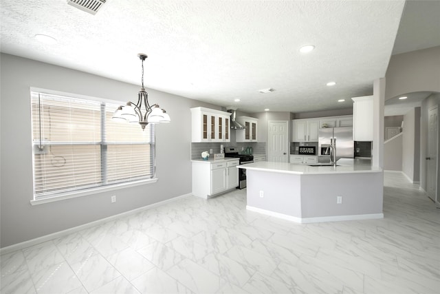 kitchen with white cabinetry, hanging light fixtures, stainless steel appliances, wall chimney range hood, and tasteful backsplash