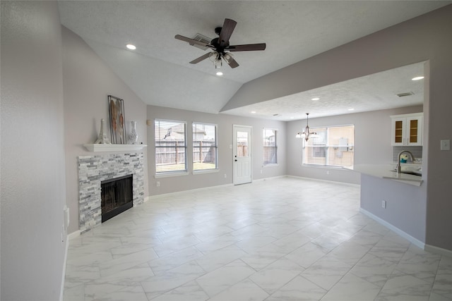 unfurnished living room featuring a fireplace, lofted ceiling, a textured ceiling, and ceiling fan with notable chandelier