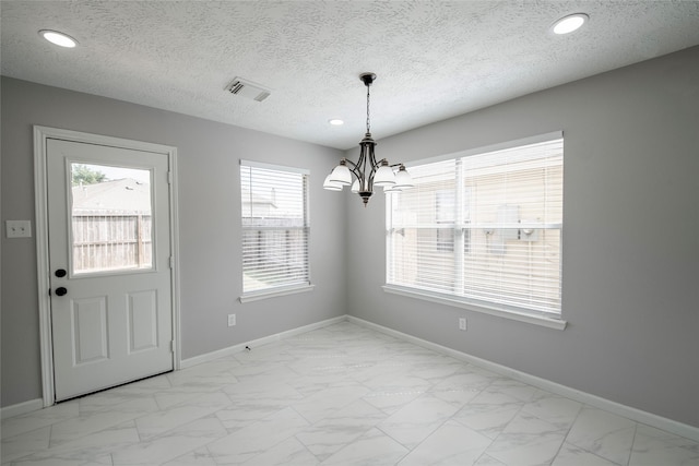 unfurnished dining area featuring a textured ceiling and a notable chandelier