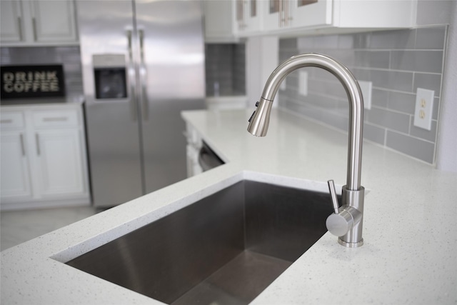 room details with tasteful backsplash, light stone countertops, white cabinets, and stainless steel refrigerator with ice dispenser