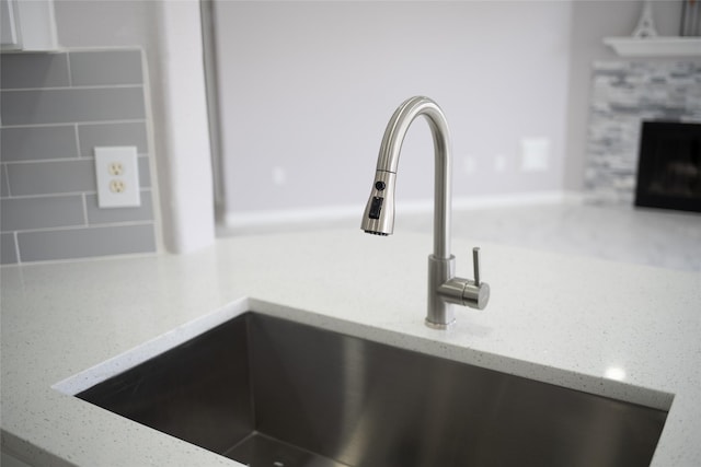 interior details featuring light stone countertops, backsplash, a stone fireplace, and sink