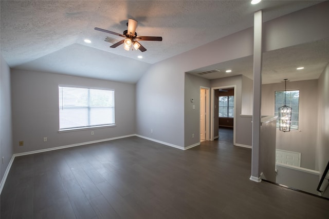 empty room with a textured ceiling, ceiling fan with notable chandelier, dark hardwood / wood-style floors, and vaulted ceiling