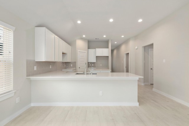 kitchen with white cabinets, sink, tasteful backsplash, light hardwood / wood-style floors, and kitchen peninsula