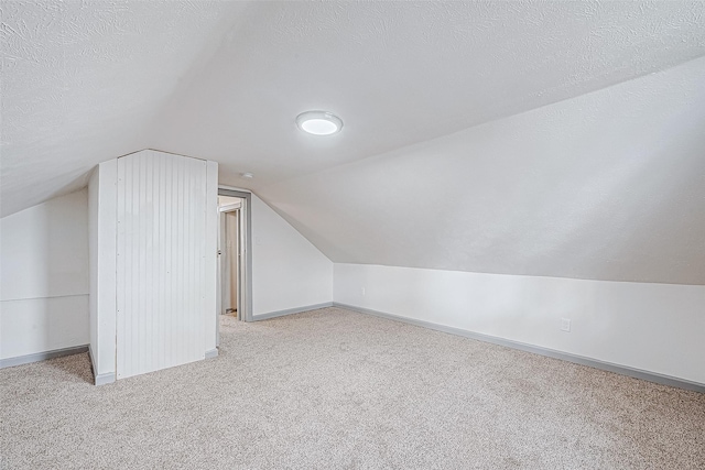 additional living space with light colored carpet, lofted ceiling, and a textured ceiling