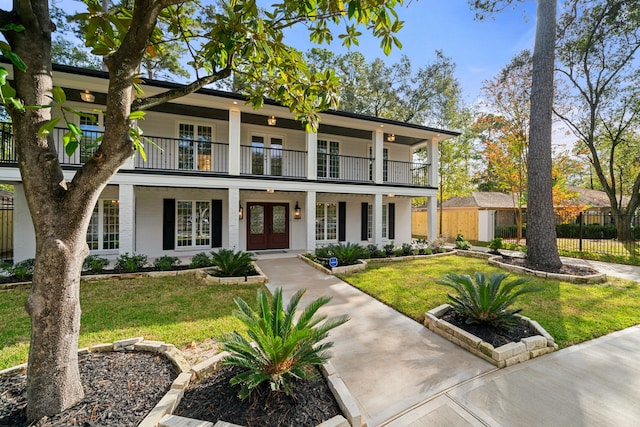 view of front of home with french doors, a balcony, and a front lawn