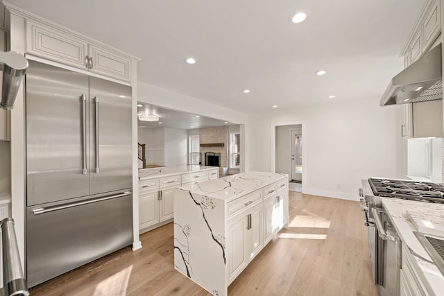 kitchen featuring high quality appliances, white cabinets, light wood-type flooring, a kitchen island, and light stone counters