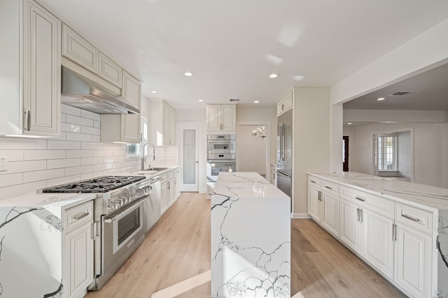 kitchen featuring exhaust hood, decorative backsplash, appliances with stainless steel finishes, a kitchen island, and light stone counters