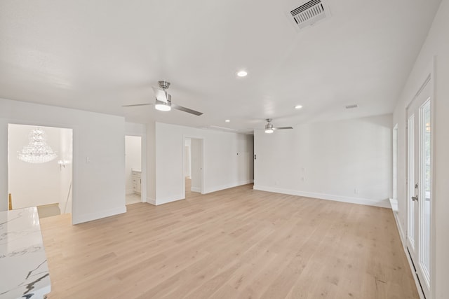 unfurnished room with ceiling fan with notable chandelier and light hardwood / wood-style flooring