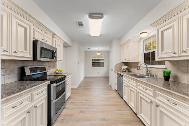 kitchen featuring decorative backsplash, appliances with stainless steel finishes, sink, cream cabinets, and light hardwood / wood-style flooring