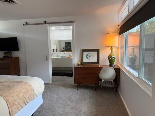 carpeted bedroom featuring a barn door, ensuite bathroom, and sink