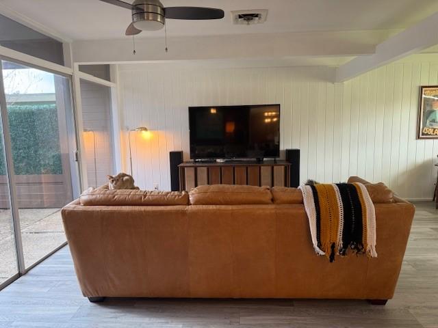 living room with beam ceiling, ceiling fan, wooden walls, and wood-type flooring