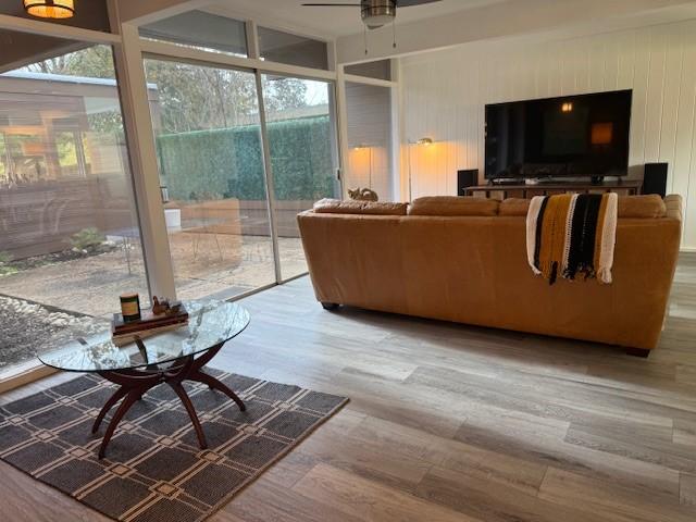 living room featuring ceiling fan, hardwood / wood-style floors, and wooden walls