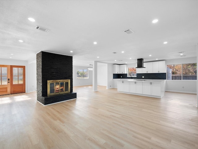 unfurnished living room with a wealth of natural light, french doors, light wood-type flooring, and a brick fireplace