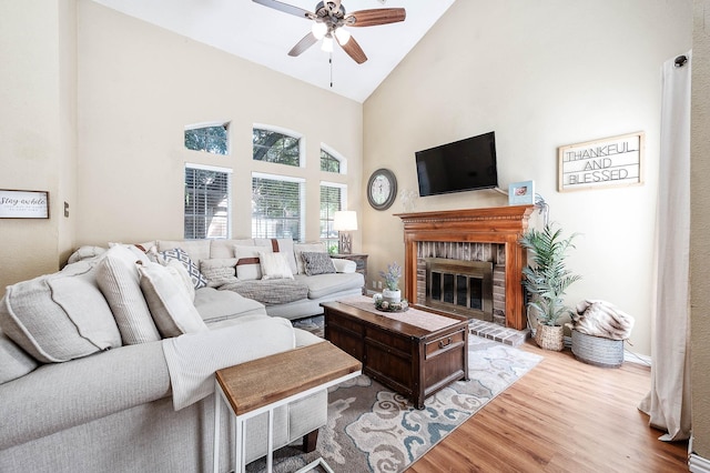 living room featuring a brick fireplace, light wood-type flooring, high vaulted ceiling, and ceiling fan