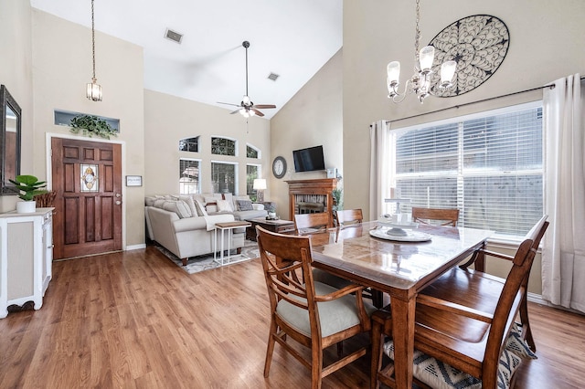 dining space with light hardwood / wood-style flooring, high vaulted ceiling, a healthy amount of sunlight, and ceiling fan with notable chandelier