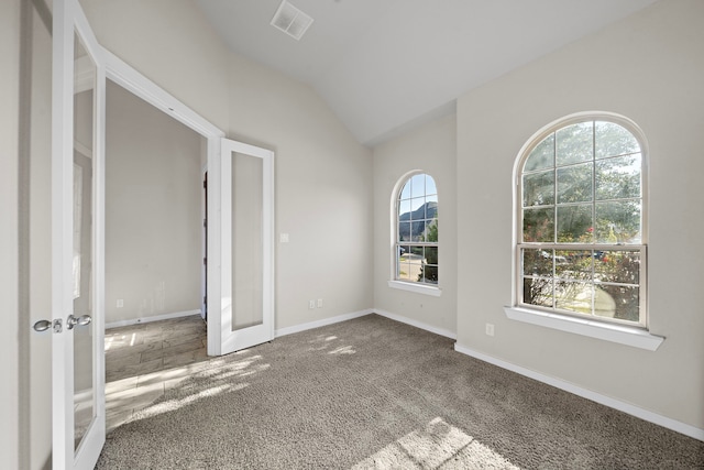 carpeted empty room with plenty of natural light, french doors, and vaulted ceiling