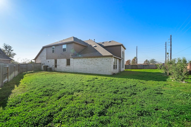 rear view of house with central air condition unit and a lawn