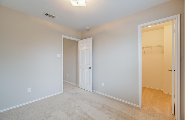 unfurnished bedroom featuring a walk in closet, light colored carpet, and a closet