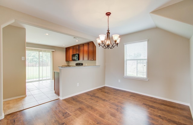 kitchen with kitchen peninsula, pendant lighting, an inviting chandelier, light hardwood / wood-style floors, and lofted ceiling