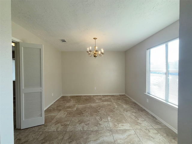 empty room featuring a chandelier, a healthy amount of sunlight, and a textured ceiling