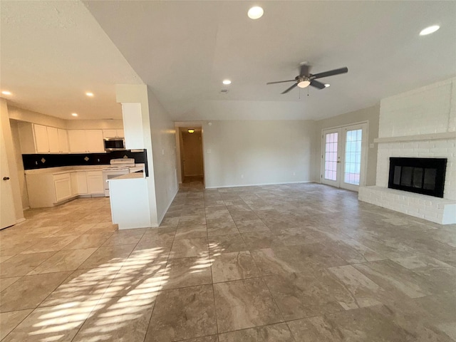 unfurnished living room with ceiling fan, french doors, and a brick fireplace