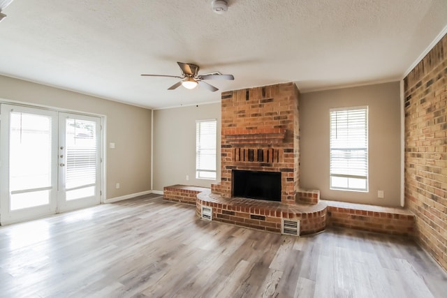 unfurnished living room with ceiling fan, french doors, a brick fireplace, light wood-type flooring, and ornamental molding