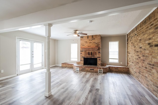 unfurnished living room featuring ceiling fan, brick wall, decorative columns, hardwood / wood-style floors, and a fireplace