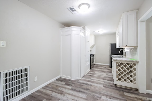 kitchen featuring light wood-type flooring, tasteful backsplash, stainless steel appliances, sink, and white cabinets