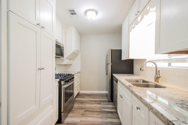 kitchen featuring light stone countertops, stainless steel appliances, sink, light hardwood / wood-style flooring, and white cabinetry