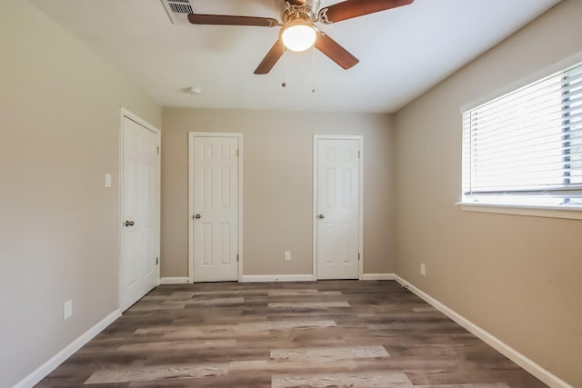 unfurnished bedroom with dark hardwood / wood-style floors, ceiling fan, and multiple closets