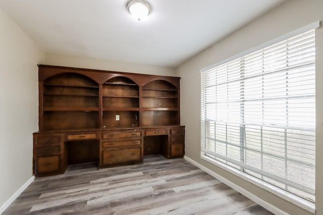 unfurnished office featuring built in desk and light hardwood / wood-style flooring