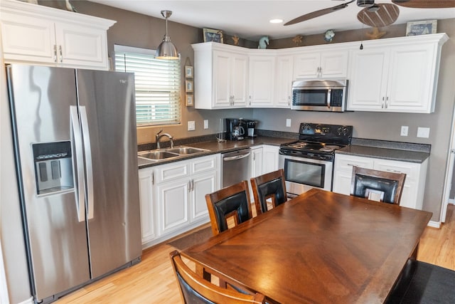 kitchen featuring appliances with stainless steel finishes, sink, light hardwood / wood-style flooring, white cabinetry, and hanging light fixtures