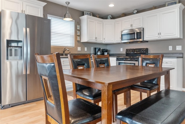 kitchen featuring sink, hanging light fixtures, light wood-type flooring, white cabinetry, and stainless steel appliances